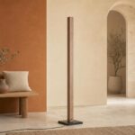 Un lampadaire avec variateur colonne bois LED 7 températures posé dans un salon beige, avec une forme fine en bois et un pied noir.