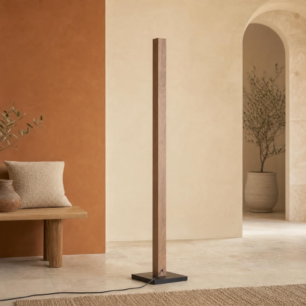 Un lampadaire avec variateur colonne bois LED 7 températures posé dans un salon beige, avec une forme fine en bois et un pied noir.